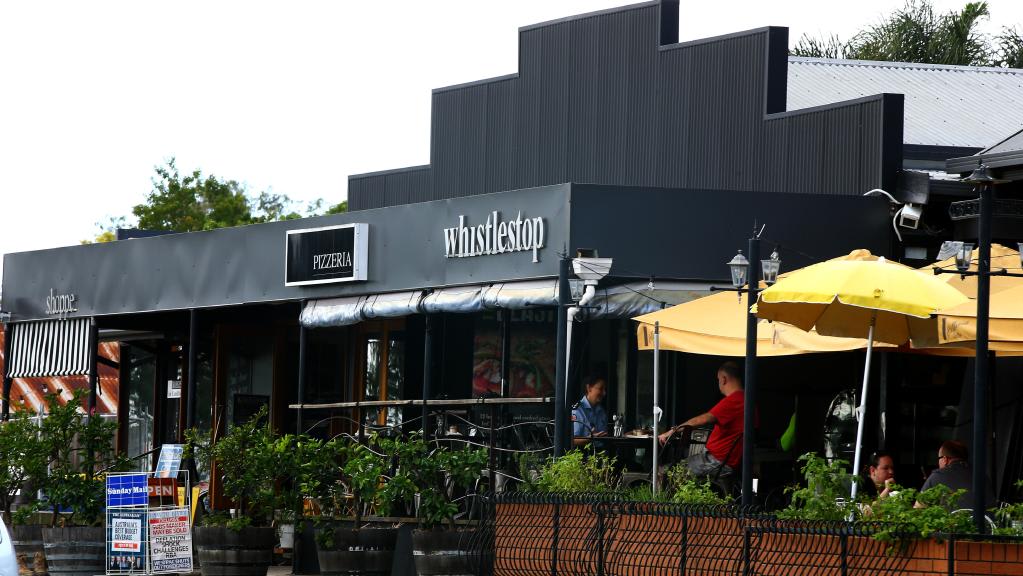Whistlestop Pimpama storefront: charcoal corrugated iron cladding with raised lowercase 'whistlestop' sign, yellow umbrellas over the outdoor dining