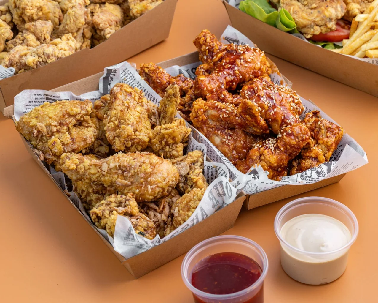 Two boxes of Haru Chicken Korean fried chicken — one plain crispy, one glazed sticky sesame — with dipping sauces
