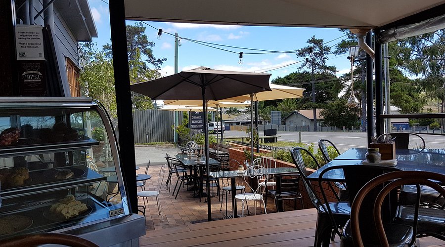 Whistlestop's timber deck with sage green bistro chairs and yellow umbrellas overlooking Pimpama Jacobs Well Road